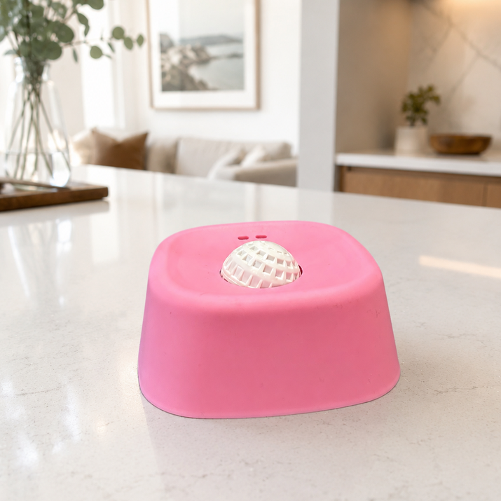 Pink dog bowl on a marble floor with a blurred indoor background