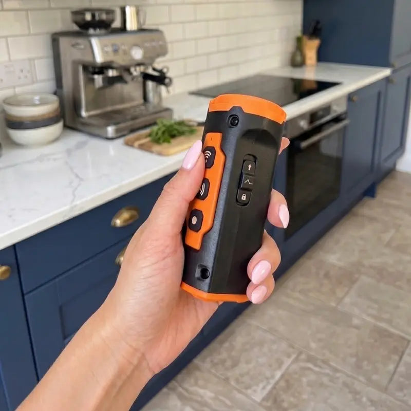 Hand holding an orange and black anti barking device in a kitchen setting