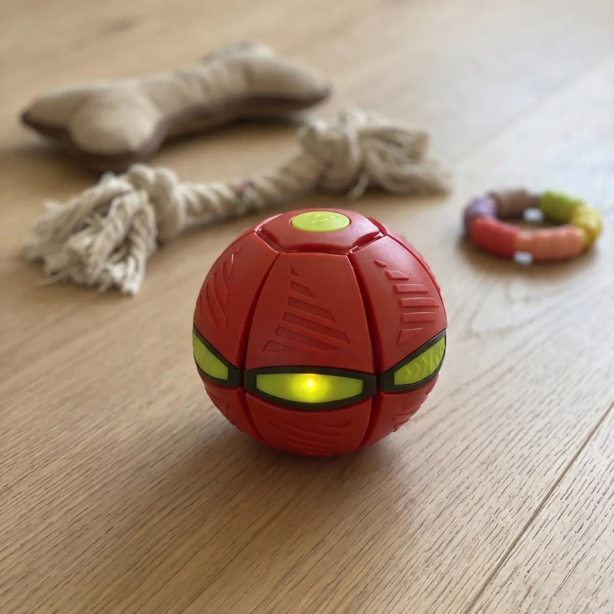 Red ball with lights on a wooden floor with dog toys in the background
