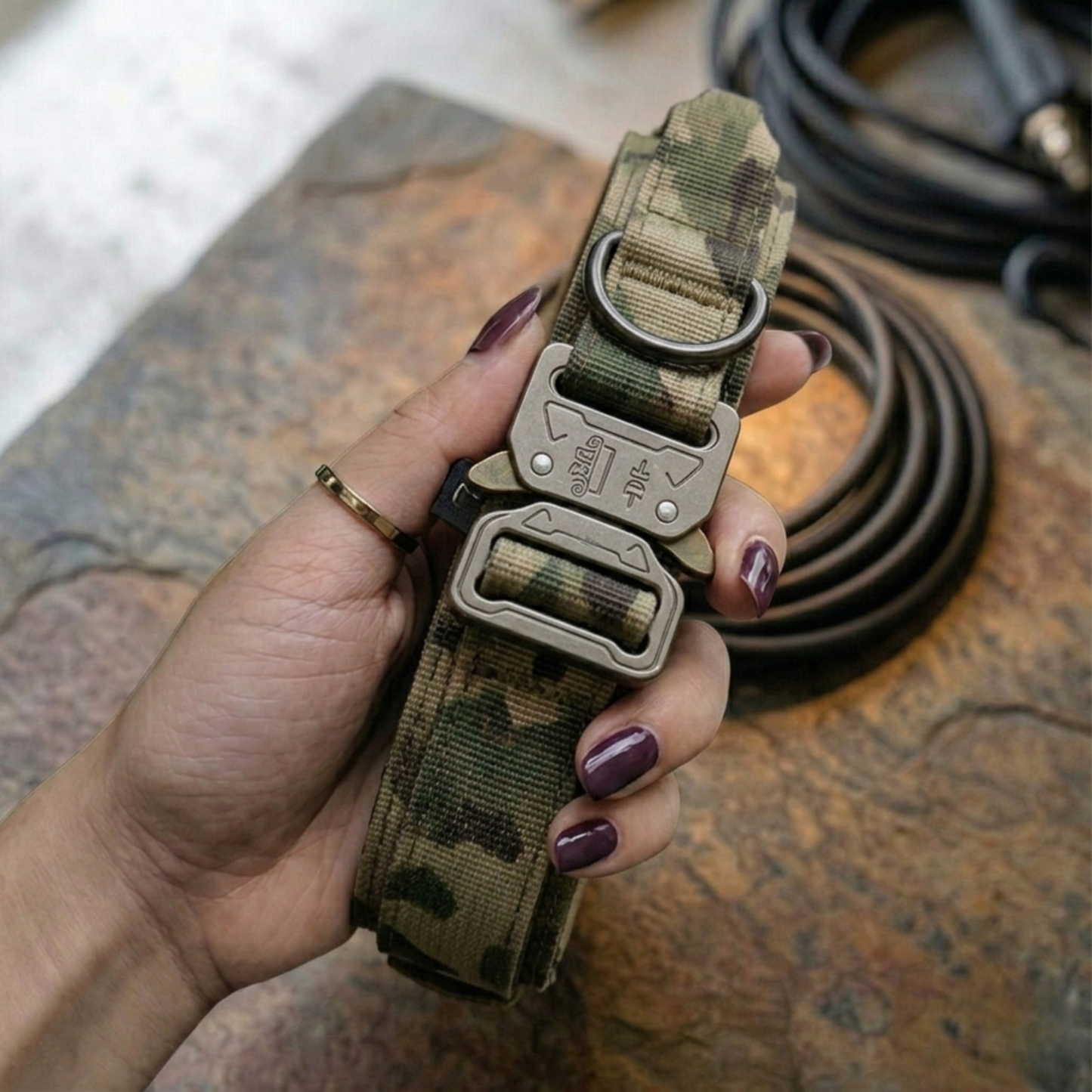 Hand holding a camouflage dog collar with metal buckle on a textured surface