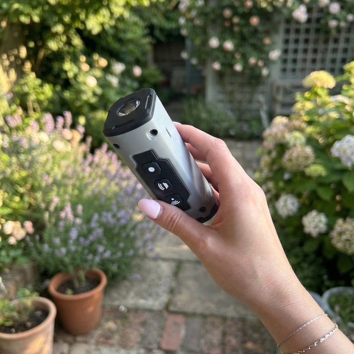 Hand holding a anti barking device with plants in the background