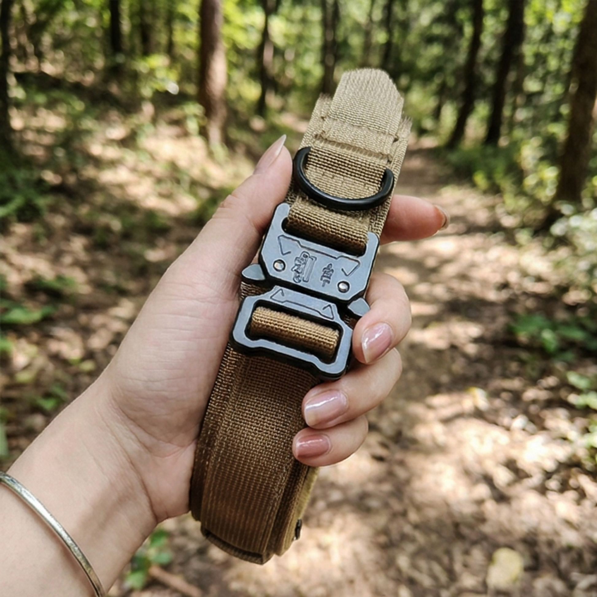 Hand holding a brown tactical belt with a black buckle in a forest setting