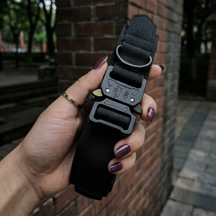 Black tactical belt with a buckle held by a hand against a brick wall background